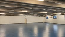 Empty room with blue floor, white walls, two doors, small windows, and ceiling lights