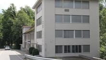 5 story building, white exterior, multiple windows, parking lot, trees in the background
