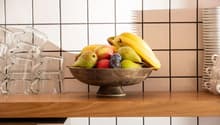 Light wooden countertop, bowl of fruits, stack of cups, tiled backsplash, oven