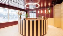 Spacious reception area with a circular wooden reception desk, decorative lighting fixtures, potted plants, and large windows providing natural light.