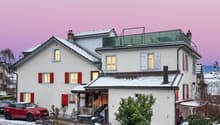 2 story house, white exterior, red shutters, snow on the roof, red car parked in front, pathway leading to the entrance, small garden with plants, fence, and a small wooden structure