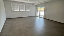 Large open living space with gray tile flooring, white walls, recessed lighting, and sliding glass doors leading to an outdoor area.