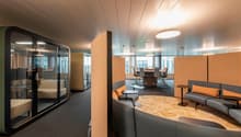 modern office space with glass walls, beige carpet, gray couches, wooden tables, and large windows