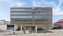 Modern office building with glass facade, multiple floors, entrance with columns, landscaped entrance area with plants and shrubs