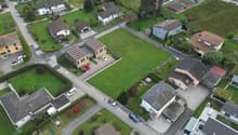 Multiple residential houses, detached garages, wide green lawns, wide roads, large open field in center