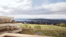 Balcony with a view overlooking a hilly, grassy landscape with a town in the distance. The apartment building has a modern, minimalist design with large windows and a terrace.