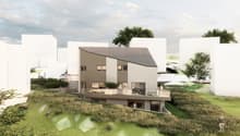 Two-story modern house with a slanted roof, wooden siding, and large windows. The house is situated on a grassy slope with trees in the background. There appears to be a balcony or terrace on the upper level.
