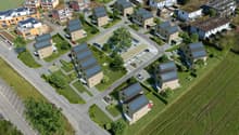 a housing development, featuring a variety of building styles and solar panels, including houses, parking garages, and green spaces with trees and grass