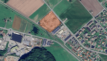 Large residential property in development with surrounding roads, nearby fields, industrial buildings, residential areas, trees, and water bodies
