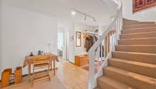 white walls, wooden floor, carpeted stairs, clothes hanging on wall, table and chair