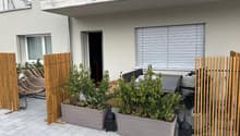 Wooden barriers with plants, tiled patio, patio furniture with plants, bicycle, white blinds, a window, an open doorway