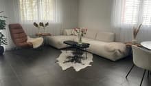 modern living room, white couch, modern black table, black tile flooring, white decorative curtains, white coffee table, large windows, two side tables, white rug, chair