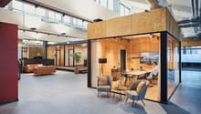 Open space office with wooden partition, glass wall, a couch, a coffee table, a plant, a table, and chairs.
