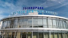 The image shows a large, modern building with a prominent sign that reads 'TECHNOPARK HIGHTECH-ZENTRUM AARGAU'. The building has a glass facade and appears to be a commercial or office space.