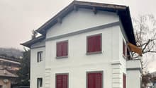 White two-story house, red shutters, beige awning, raised ground floor, entrance to the right