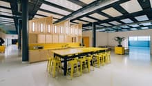 large open room with yellow counters and barstools, kitchen area with modern appliances, industrial style ceiling