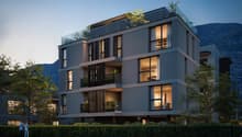 Modern multi-story building with glass balconies, illuminated windows, and a rooftop terrace with greenery.
