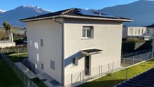 Modern 2 story house, solar panels on the roof, white exterior, fenced garden, mountains in the background