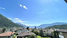 Town with mountains in the background, brick houses, tiled roofs, a car parked in front of one house, another car parked in a garage.