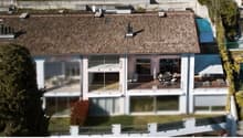 Aerial view of a modern house with a brown roof, glass windows, and balconies.