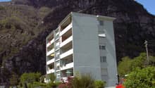 Multi-story building with multiple balconies, located at the base of a rocky mountain with steep slopes