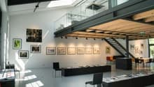 High ceiling, gallery-style space, glass railings, skylights, mounted pictures, furniture in a neat manner