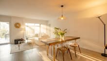 modern living room with white walls, wooden table, white couch, floor lamp, round mirror, floor to ceiling windows, rug, plants