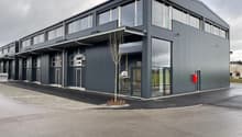 Exterior shot of a building with multiple units, grey exterior, multiple windows, paved area in front