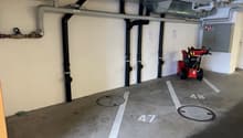 Underground parking garage with floor numbered parking spaces and pipes along the walls.