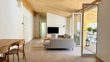 modern living room with wooden table, gray sofa, flatscreen TV, beige rug, wooden ceiling