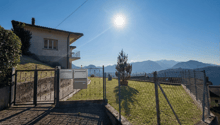 House with a balcony, surrounded by a fence, with a mailbox, a small garden, and a view of the mountains.