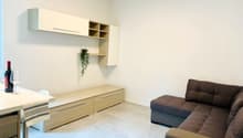 modern living room with white walls, wooden floor, a couch, a bench, a wine bottle, wine glasses, a plant, and a white table