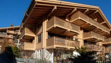 Modern wooden apartment building with multiple balconies, large windows, and a sloped roof