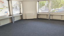 Empty room with three windows, grey carpet, radiators, ceiling lights