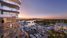 High-rise building with glass balconies, overlooking a marina with many boats and yachts, city skyline in the distance