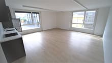 empty room, wooden floor, white walls, large windows, kitchen area with sink and stove