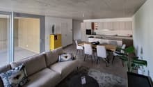 Open plan living and dining area with modern furniture, large windows, and a yellow storage unit.