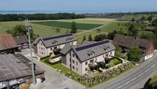 Aerial view of a residential complex with two houses, solar panels on the roofs, a garden, and a road.