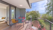 Balcony with wooden floor, metal railing, table and chairs, glass doors, couch, view of trees and mountains