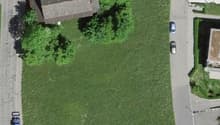 Aerial view of a residential area with a large green field, several houses, and parked cars.