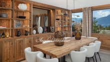 Dining room with wooden table, white chairs, wooden shelves, large windows, mountain view