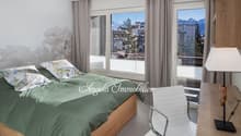 large bed, green linens, pillows, gray curtains, white walls, desk, chair, lamp, balcony, mountain view