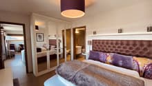 Bedroom with a large bed, a large wardrobe, a mirror, a lamp, a desk, and a chair.