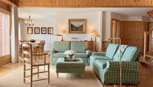 living room with wooden ceiling, green and white checkered sofas, wooden table, wooden chair, wooden floor, dining table and chairs, wooden cabinet, lamps, picture frames, chandelier