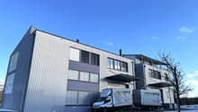 Commercial building, grey and purple color, large window glass, trucks parked in front
