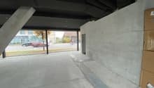 concrete wall, ceiling with beams, open parking area, person riding a bike on road