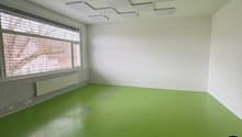 Empty room with green floor, white walls, large window, and ceiling panels