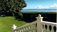 white wooden railing, green lawn, large tree, beach and ocean visible