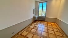 Empty room with wooden parquet flooring, white walls, a window, a small sink with a mirror, and a radiator.