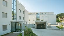 Multi-story apartment building with a garage entrance, glass windows, and landscaping around the entrance.